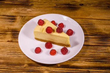 White plate with cheesecake New York and raspberries on wooden table