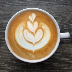 Foto op Plexiglas Top view of a mug of latte art coffee on timber background. © tanarch