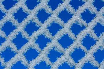 Chain link fence covered with hoarfrost over blue sky background
