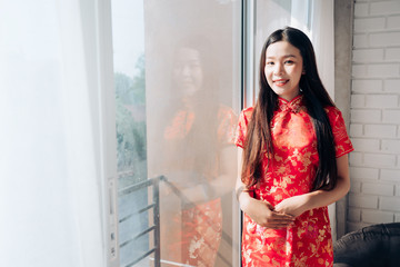 Smile of Portrait Beauty Asian Woman with Chinese dress,Qipao,Cheongsam Chinese New Year Standing near Window in Clean White Room.