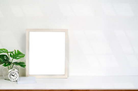Mock up white wooden frame with blank page and houseplant on white table and white background