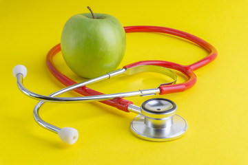 Green Apple with medical stethoscope isolated on yellow background for healthy eating. Selective focus and crop fragment. Healthy, Diet and copy space concept