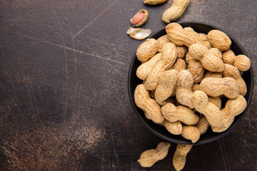 Peanuts in shell in bowl on dark background. Healthy food, whole untreated nuts, tasty snack