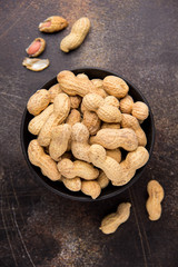 Peanuts in shell in bowl on dark background. Healthy food, whole untreated nuts, tasty snack