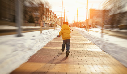 The little boy is running through the winter boulevard