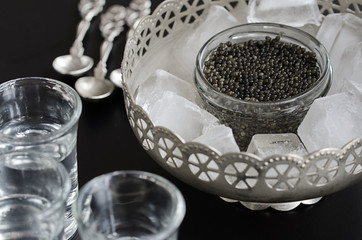 Russian beluga caviar served in silver bowl with ice and vodka. Black caviar delicatessen...