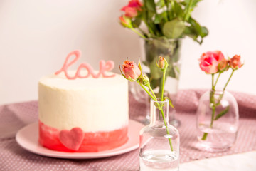 White cake with pink decor and the word love on top among small white and pink roses. Valentine's Day Gift Concept