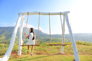 Happy young woman relaxing by swing on hillside at morning sunrise.