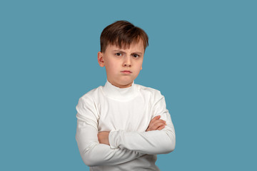 Close up  portrait of a serious or angry boy wearing white shirt with arms crossed on blue background in studio