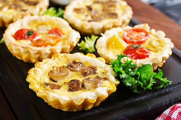 Mushrooms, cheddar, tomatoes tartlets on wooden background. Mini pies. Delicious appetizer, tapas, snack.