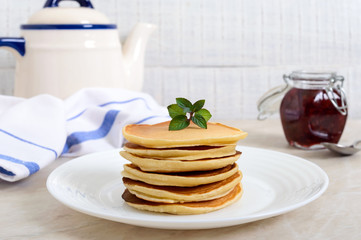 Delicious pancakes with raspberry jam on a white plate on the kitchen table. Classic American homemade breakfast.