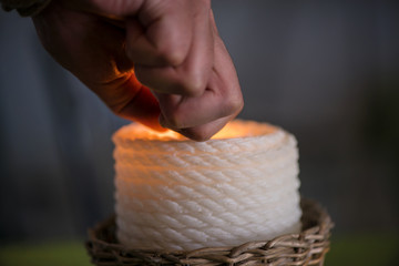 Candle in wicker wooden basket standing on table in restaurant or dining room on green, natural linen tablecloth being lit up. Romantic atmosphere for couples, time for dinner. Cosy home, clean sheets