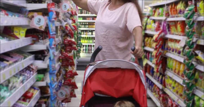 Happy mature woman holding charming boy baby rolls in a stroller while buying products in market together