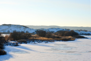 Aerial view of sunset over winter snow-covered river or lake, hills and forest. 