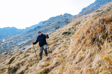 Fototapeta premium The young man of sporting physique rises to the mountain with sporting equipment