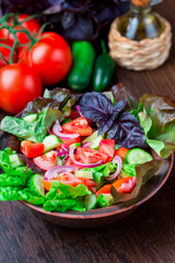 Salad with fresh vegetables, garden herbs and sun-dried tomatoes in a clay bowl on a dark wooden background