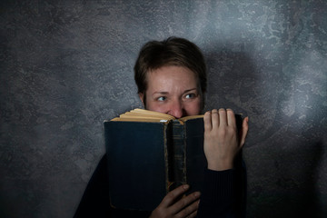 Portrait of a woman covering her face with a book, on a dark textural background in the studio.