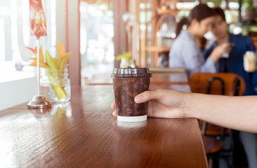 Woman hand holds out a paper cup of coffee to take away.