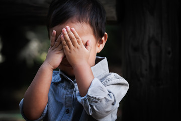 A young boy of toddler age covering his face with hands, showing signs of distress, fear and...