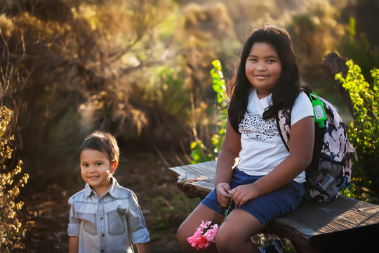 A boy and his older sister are sitting down, taking a break during a hike or field trip while the sun is setting.