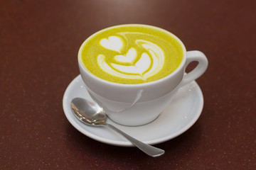 A cup of green tea matcha latte with heart latte art on top.