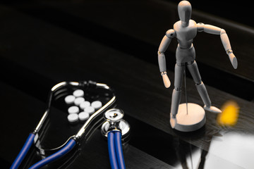 Pills, a stethoscope and a fake person on a black background