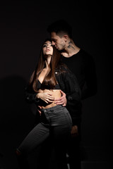 Guy and girl dressed in black clothes are passionately hugging in a dark room