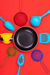 Frying pan in the center with cooking utensils around isolated on red background