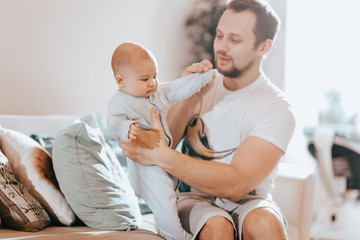 Fototapeta premium Young father holds his tiny sun on the sofa in the light room