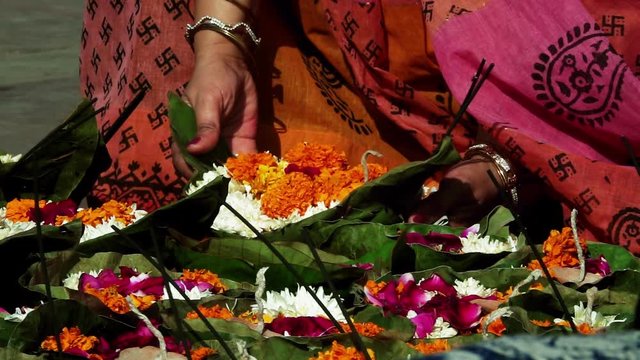 Slow motion shot of a lady picking up worship material (Puja Samagri) for worshipping Holy Ganges River (Ganga) at Har Ki Pauri, Haridwar, Uttarakhand, India. It includes flowers, candles. 
