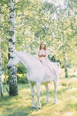 Aerial photo shoot at sunset in the forest with a horse. A girl in a flying dress with a unicorn.