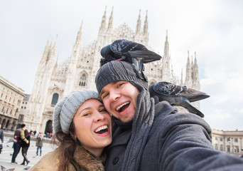 Fototapeta na wymiar Travel, Italy and funny couple concept - Happy tourists taking a self portrait with pigeons in front of Duomo cathedral, Milan