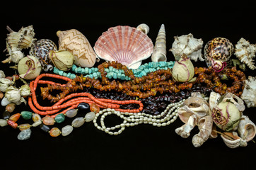 Fototapeta premium Beads of turquoise, red coral, amber, garnet stone, multi-colored agate, pearls among various shells and dry buds on a black background 