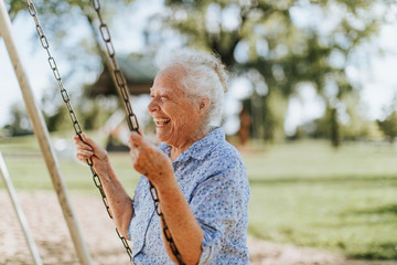 Cheerful senior woman on a swing at a playground - obrazy, fototapety, plakaty