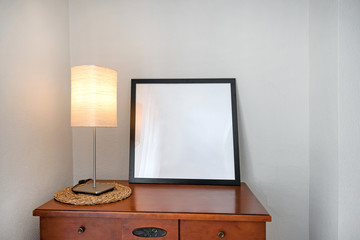 Lit up vintage look night lamp standing on tv table next to white, empty frame. Space for text, logo, drawing or art. 