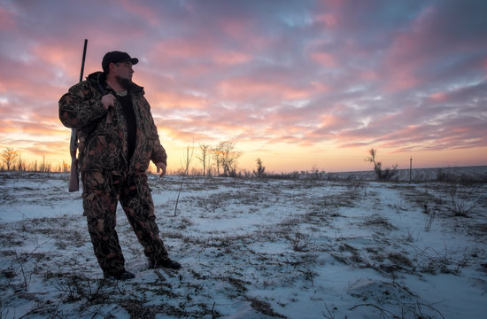 Winter hunting at sunrise. Hunter moving With Shotgun and Looking For Prey.