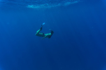 Young woman swimming underwater in blue sea with sun rays