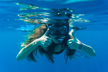 Young woman snorkeling making thumbs up signs underwater near coral reef in blue sea. Underwater.