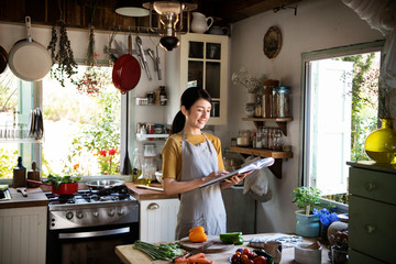 Happy woman reading a cookbook in the kitchen