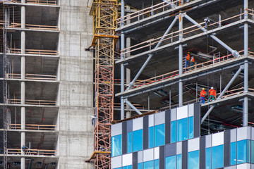 New residential and office block buildings being constructed. Industrial building site. Workers putting windows in under construction skyscraper. 