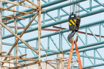 Fototapeta premium Black and yellow crane hook lifting steel truss structure at construction site. Equipment for construction industry.