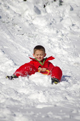 Fototapeta na wymiar vacances d'hiver - enfant en combinaison rouge faisant de la luge