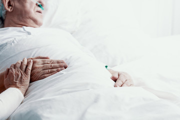 Obraz na płótnie Canvas Elderly man suffering form pancreatic cancer, laying in hospital bed, helping and on his hand as symbol of support, photo with copy space