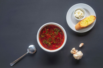 Ukrainian borsch with sour cream and toast in a bowl on a dark background