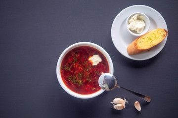 Ukrainian borsch with sour cream and toast in a bowl on a dark background