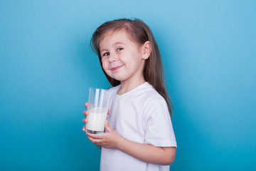 Cute little girl drinking milk from glass on blue background