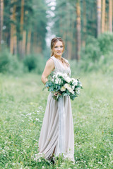 Fototapeta premium Boudoir photo shoot of the bride in the woods with a bouquet. Flying dress and beautiful girl in the Park.