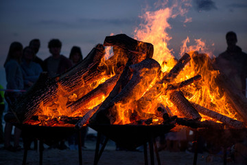 Large burning bonfire with soft glowing flame and sparkles flying all around. Romantic summer evening, people relaxing and enjoying calmness at the seaside during the Night of ancient lights.  