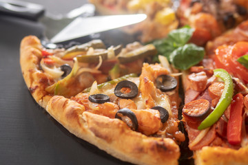 Pizza with ham, orange and red pepper, cherry tomatoes, black olives, mushrooms and fresh basil. Italian pizza. Symbolic image. Concept for a tasty and healthy meal. Selective focus. Close up.