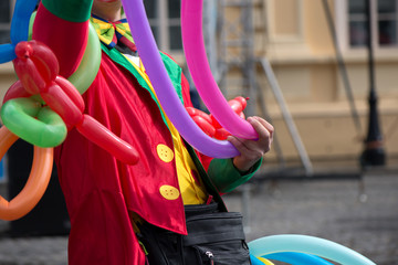 Fototapeta na wymiar A freelance clown creating balloon animals and different shapes at outdoor festival in city center. School bag, angel wings, butterflies and dogs made of balloons. Concept of entertainment, birthdays